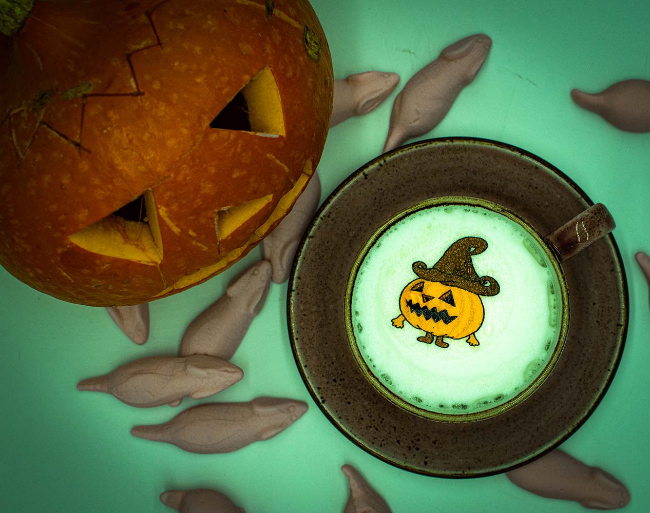 Oben links ist ein geschnitzter Halloween Kuerbis. Der Boden ist bedeckt mit Süßigkeiten und in der Kaffee Tasse ist ein gruseliger Kuerbis Sticker
