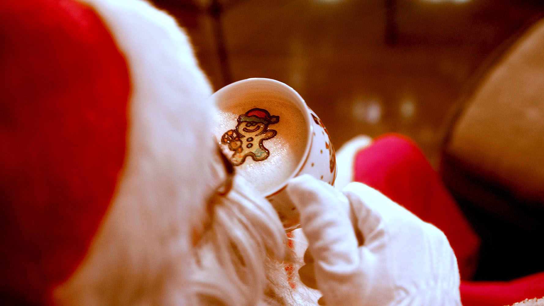 Weihnachtsmann im Kostuem von hinten mit Kaffeetasse in der Hand. Auf dem Schaum ist ein Lebkuchenmann Sticker