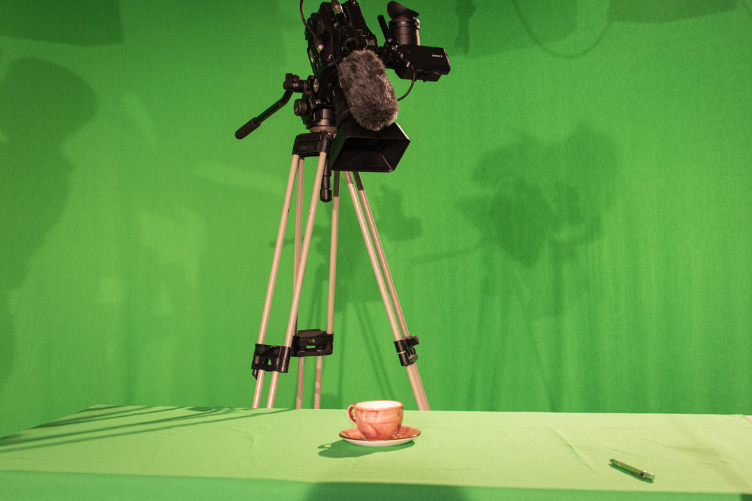 Eine Filmkamera zielt auf eine rote Tasse die auf einem Tisch steht. Im Hintergrund ist ein Greenscreen zu erkennen