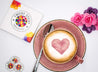 Twicky Sticky geometrisches Herz in roter Tasse mit Kaffee. Faltschachtel liegt neben der Untertasse und bunte Rosen sind rechts im Bild.